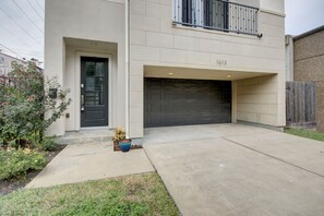 A modern two-story house with a garage, a front door, and a small balcony. - 4Story Home w/ Rooftop in Heights & Yale - Corporate Housing Rental (Houston)
