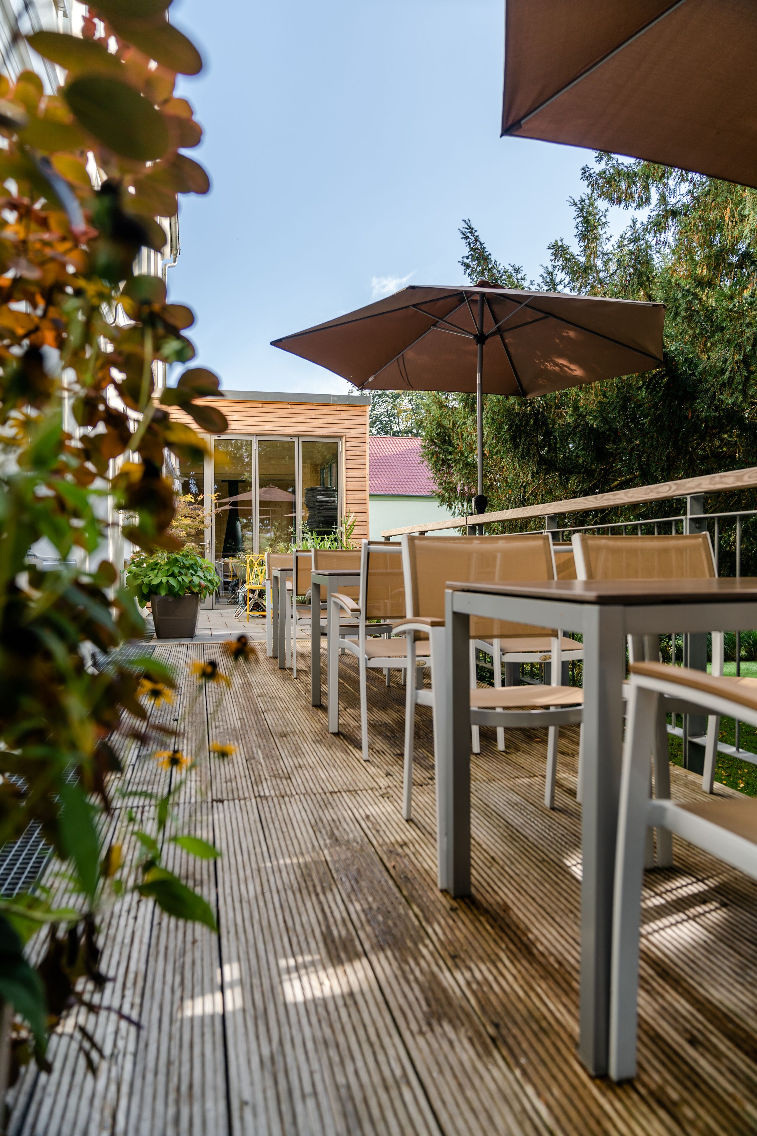 An outdoor patio with wooden flooring, metal chairs, and a table under a large umbrella.