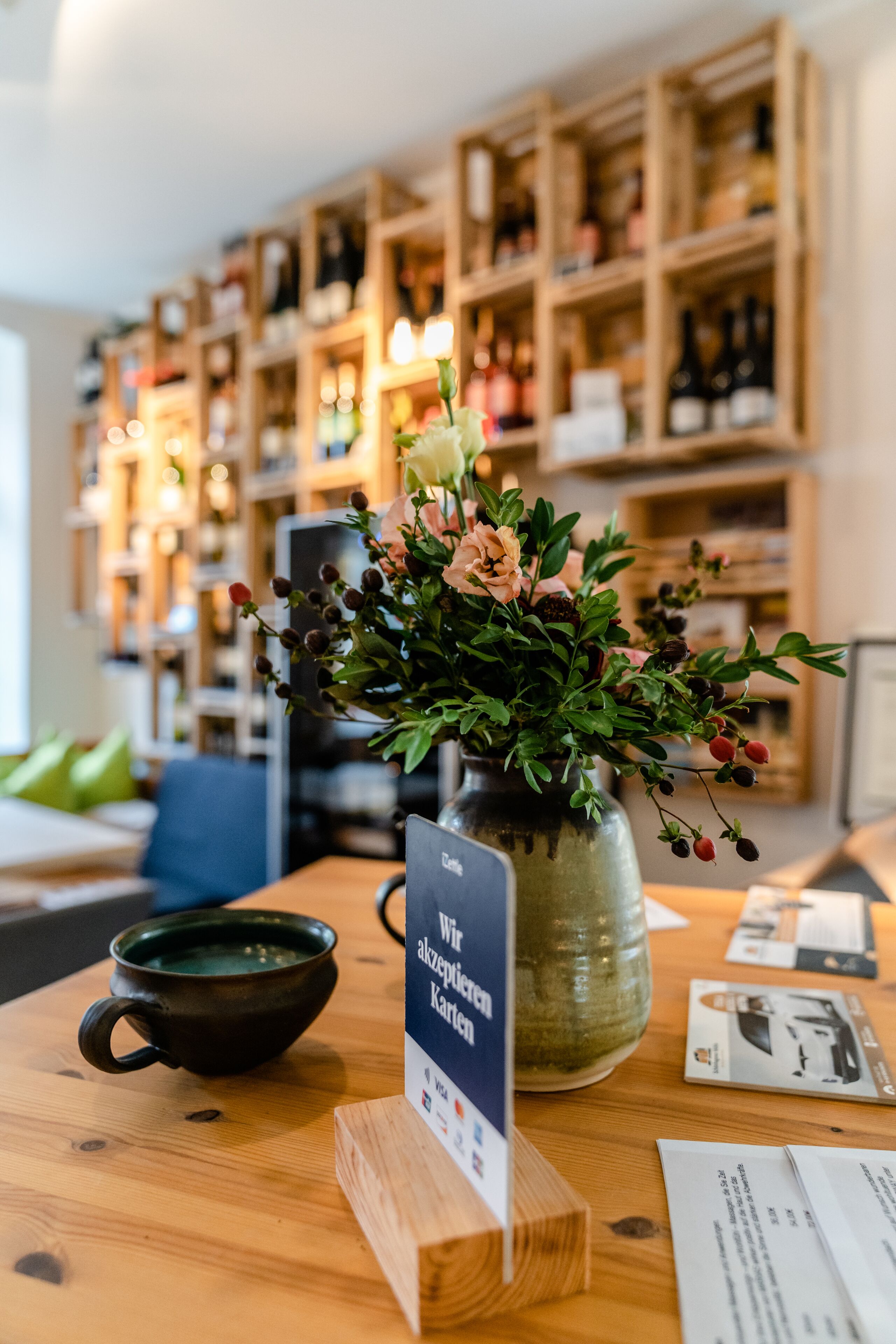 A wooden table with a vase of flowers, a black mug, and a sign with text.