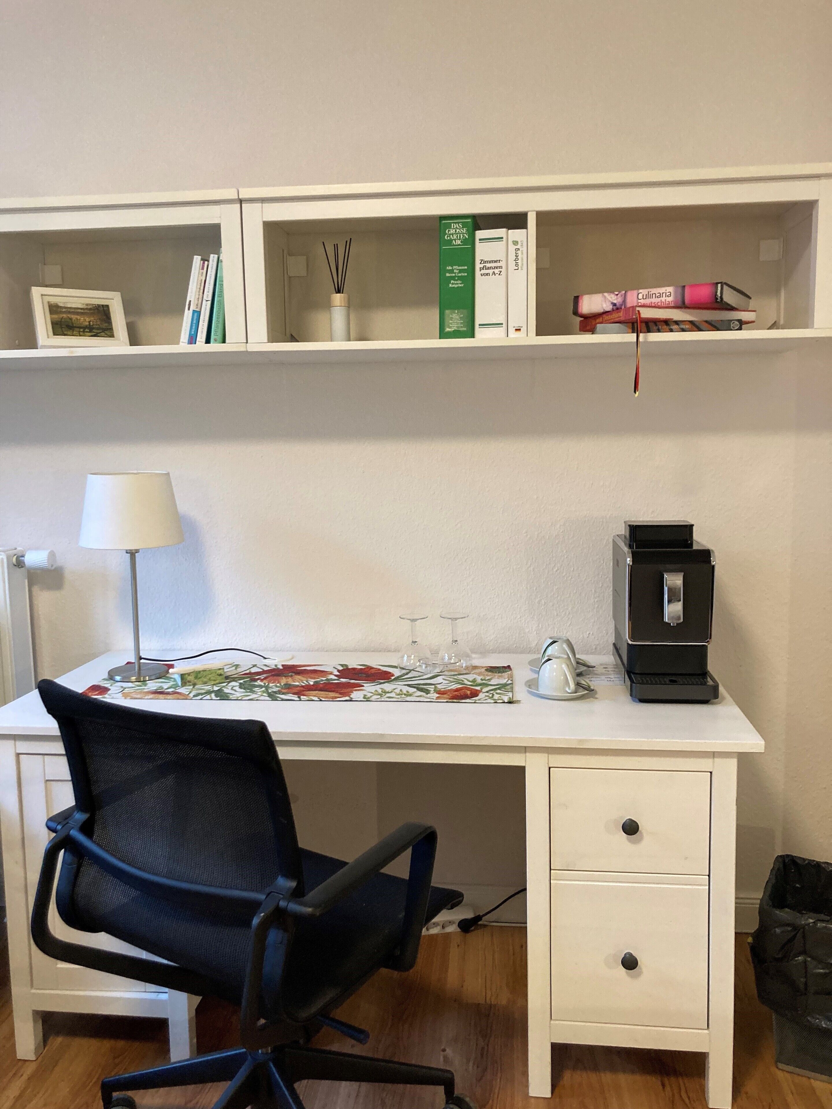 Un bureau avec une chaise, une lampe, une machine à café et des étagères remplies de livres et d’objets décoratifs.