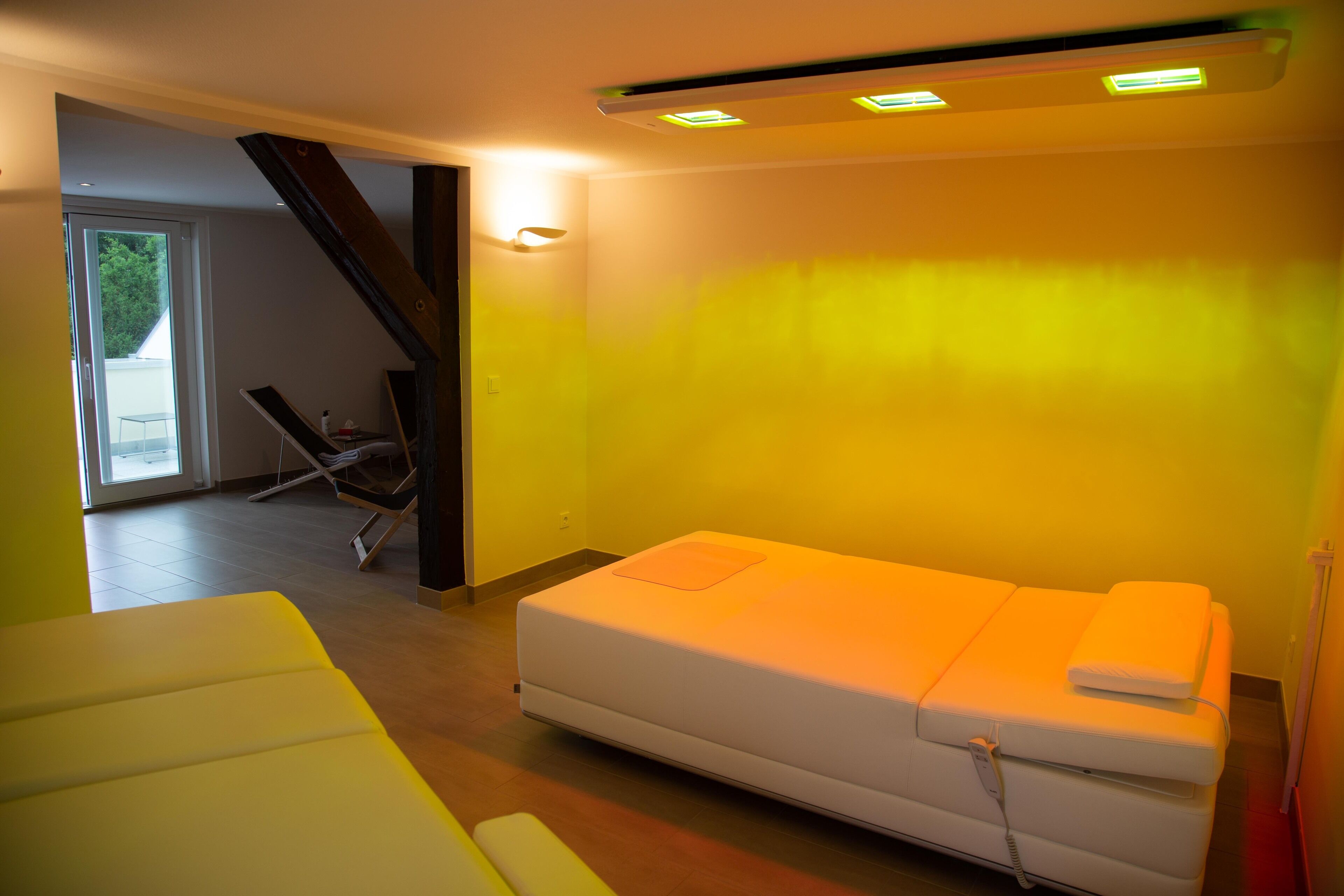 A room with a single bed, a small table, and a chair. There is a staircase leading to an upper level.