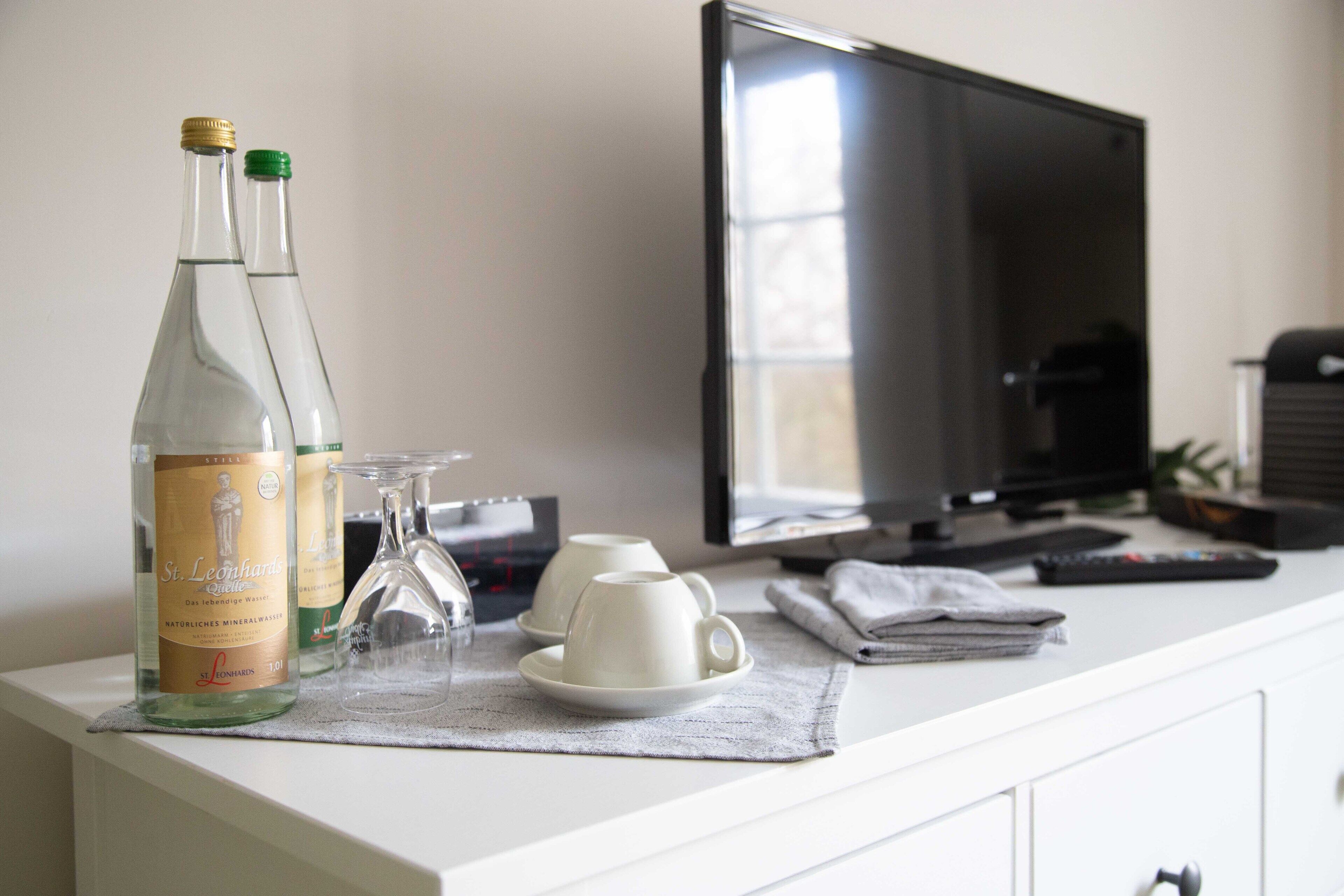A white minibar with two bottles of St. Leonhard's mineral water, a glass, and a white cup on a placemat.