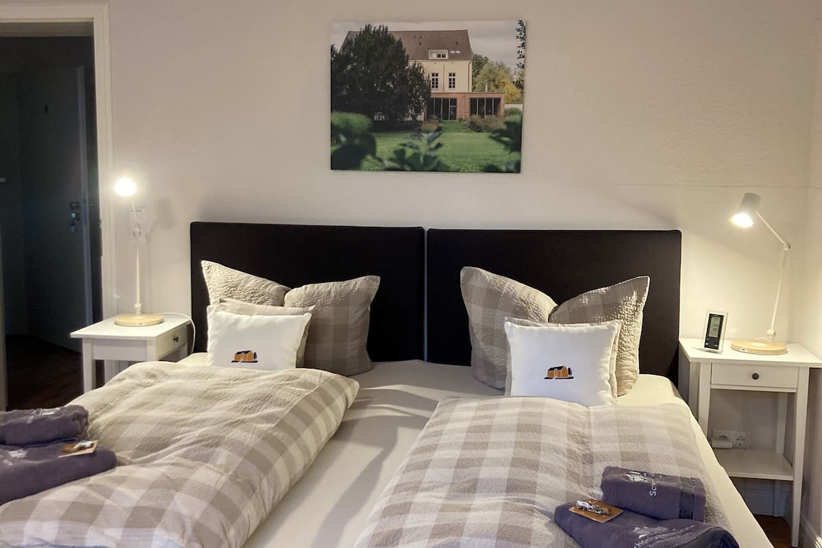 Ein Doppelbett mit kariertem Überwurf, zwei Nachttische mit Lampen, ein Beistelltisch und ein gerahmtes Bild an der Wand.