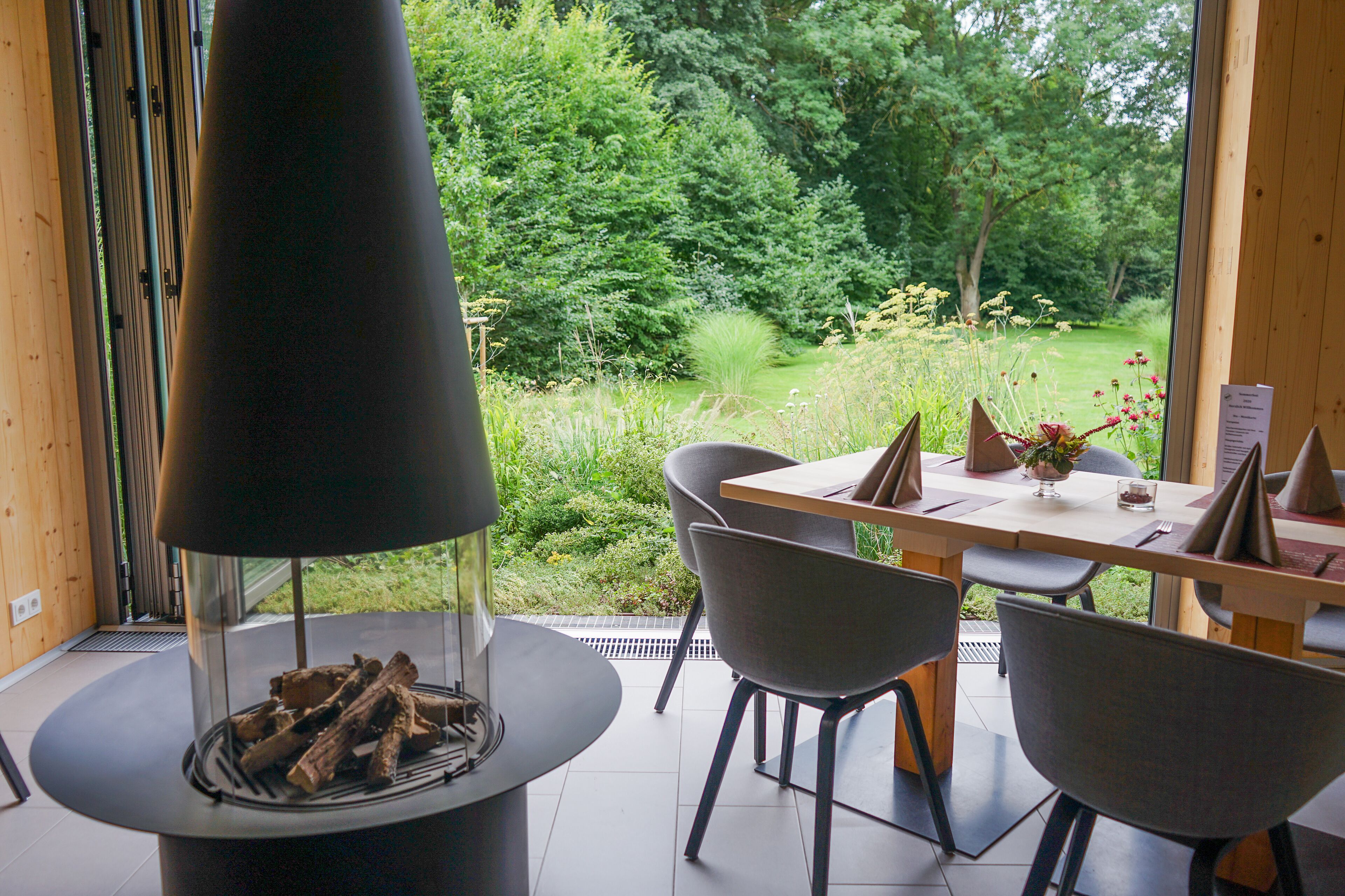 Ein moderner Essbereich mit Kamin aus Glas, einem Holztisch und grauen Stühlen.