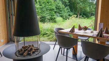 Ein moderner Essbereich mit Kamin aus Glas, einem Holztisch und grauen Stühlen.