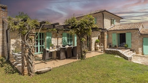 A stone house with a patio, green shutters, and a garden. - Le Chateau (Visnjan)