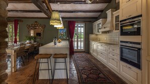 A spacious kitchen with a central island, wooden beams on the ceiling, and a large window with red curtains. - Le Chateau (Visnjan)