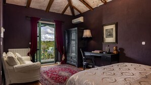 A bedroom with a bed, a desk, a chair, a radiator, a window with curtains, a framed picture, and a view of greenery outside. - Le Chateau (Visnjan)