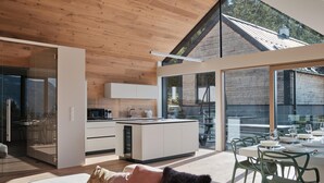 Une cuisine moderne dotée d’un îlot central, d’un coin repas avec une table et des chaises, et d’un espace salon confortable avec un canapé et des coussins.