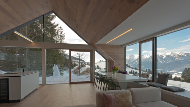 Un intérieur moderne avec de grandes fenêtres, un plafond en bois, un canapé et un coin repas avec des chaises.