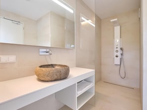 Une salle de bain moderne avec un lavabo en pierre, une douche en verre et un meuble-lavabo blanc.