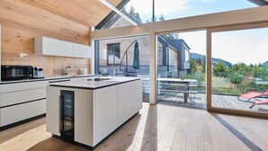 Une cuisine moderne dotée d’un grand îlot central, de planchers en bois et offrant une vue sur une terrasse et un espace extérieur.