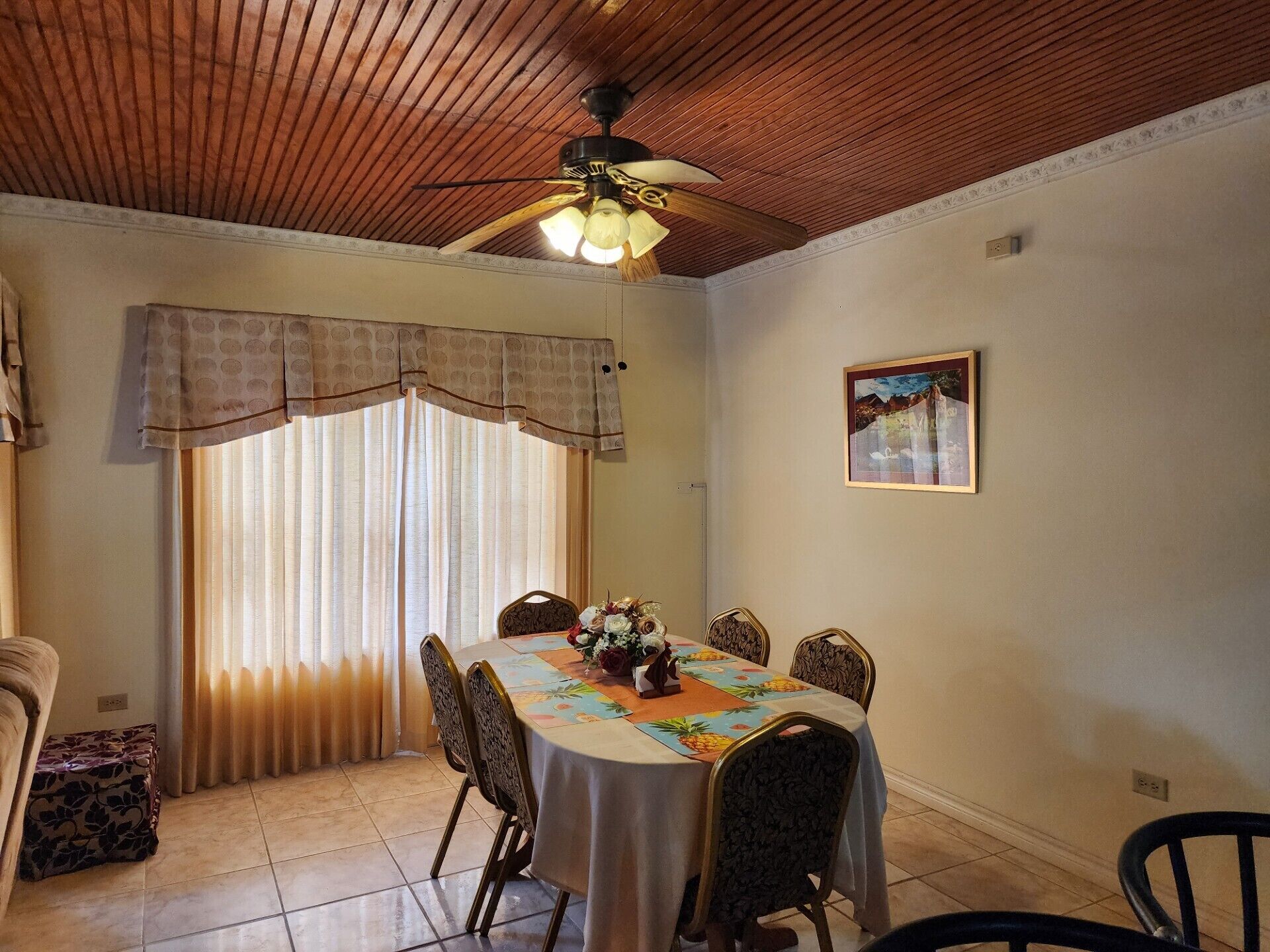 Un coin repas comprenant une table ronde, des chaises, un ventilateur de plafond et une fenêtre avec des rideaux.