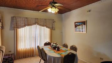 Un coin repas comprenant une table ronde, des chaises, un ventilateur de plafond et une fenêtre avec des rideaux.