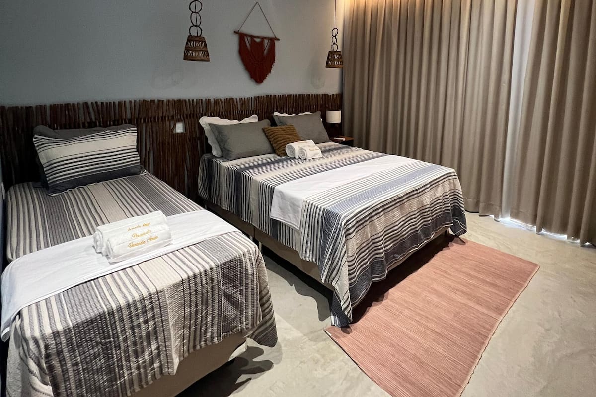 Une chambre d’hôtel avec deux lits, une grande fenêtre avec des rideaux, un luminaire au plafond et des éléments de décoration fixés au mur.