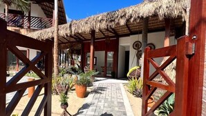A tropical resort with a thatched-roof structure, a paved pathway, and palm trees. - Pousada Varanda Amar (Amontada)