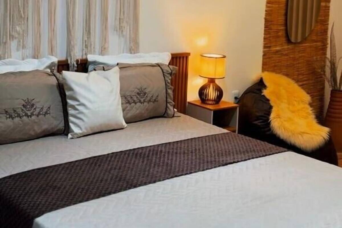 Une chambre d’hôtel avec un grand lit, une table de chevet avec une lampe, une chaise et un panneau décoratif au mur.