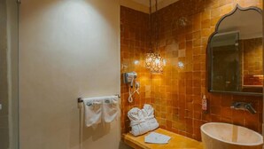 Une salle de bain avec un mur carrelé, un lavabo, un miroir, un porte-serviettes et une robe posée sur le comptoir.