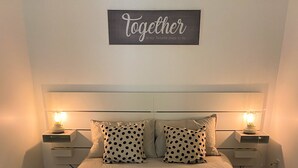 A neatly made bed with a light-colored duvet, two bedside tables with lamps, and a sign above stating "Together is my favorite place to be."