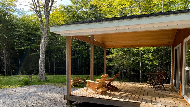 A wooden deck with outdoor seating, surrounded by a forested area.