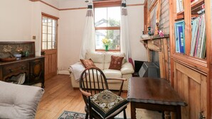 A cozy room with a wooden floor, a white sofa, a wooden chair, a table, and a bookshelf filled with books. - Oakman Cottage (Honiton)