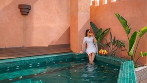 A woman in a white dress standing in a pool with a wooden deck and tropical plants. - Riad Lalla Mimouna - Suite (Marrakech)