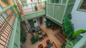 An indoor courtyard with a tiled floor, green railings, and wicker furniture. - Riad Lalla Mimouna - Suite (Marrakech)