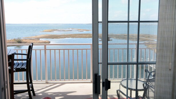 A room with a view of a lake and a balcony with a table and chairs.