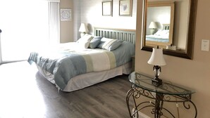 A bedroom with a bed, a ceiling fan, a large mirror, and a glass table.