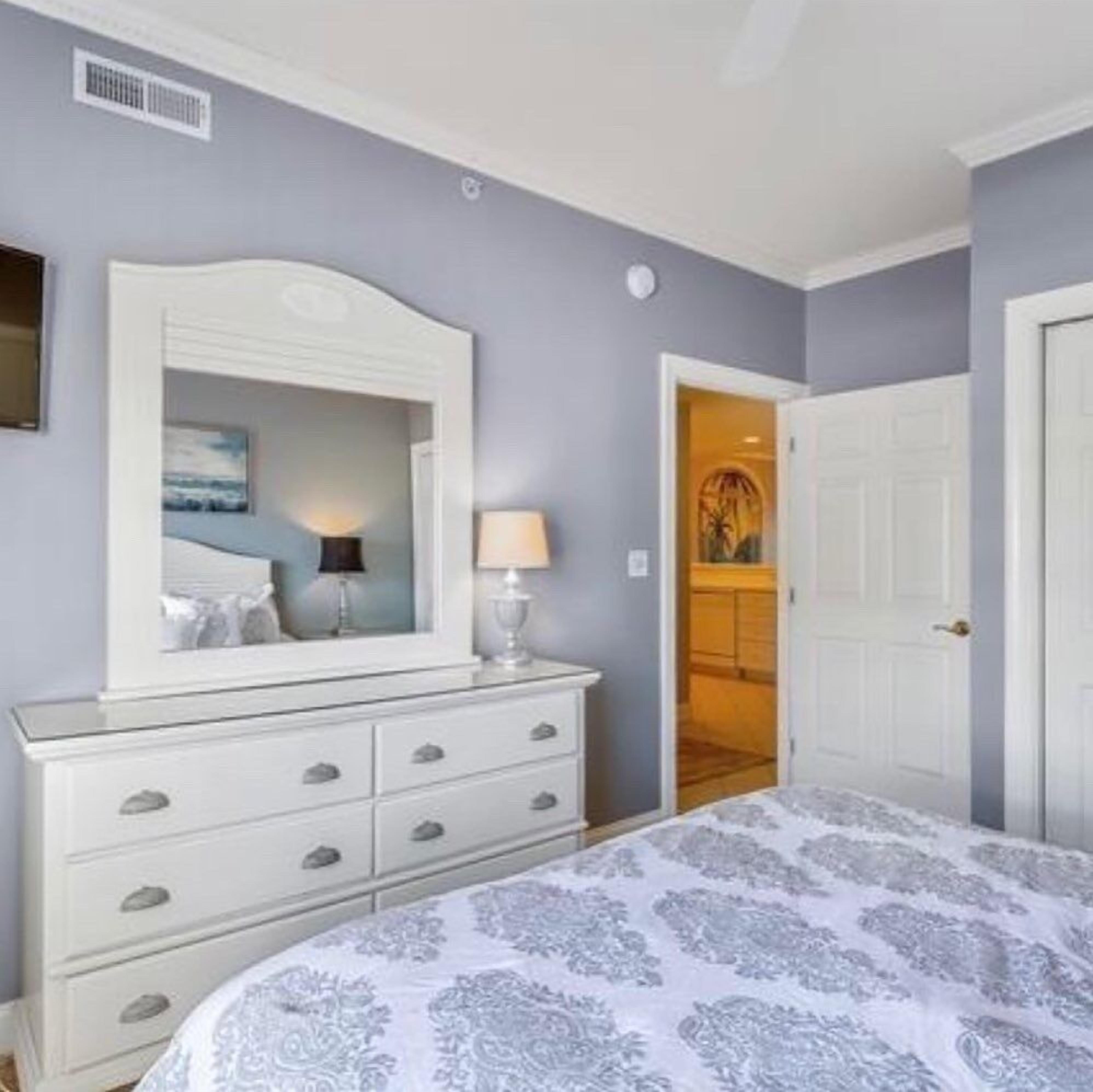 A bedroom with a bed, dresser, mirror, and a door leading to a bathroom.