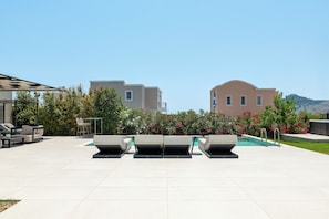 A rooftop pool area with lounge chairs, a table, and a view of buildings and mountains.