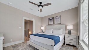 Une chambre à coucher comprenant un lit, des tables de chevet, un ventilateur de plafond et une fenêtre avec des stores.