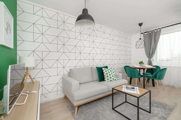 A stylish living room with a white geometric-patterned wall, a grey sofa, and a small table.