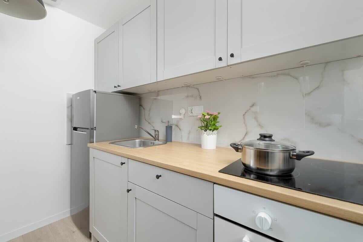 A modern kitchen with white cabinets, a stainless steel refrigerator, a sink, and a stove with a pot on it.