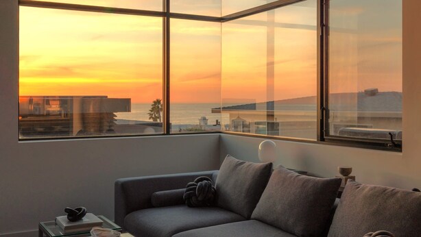 A modern living room with a large window offering a sunset view of a cityscape and water. - Ocean View | Steps to DT Manhattan Beach|King Beds (Manhattan Beach)