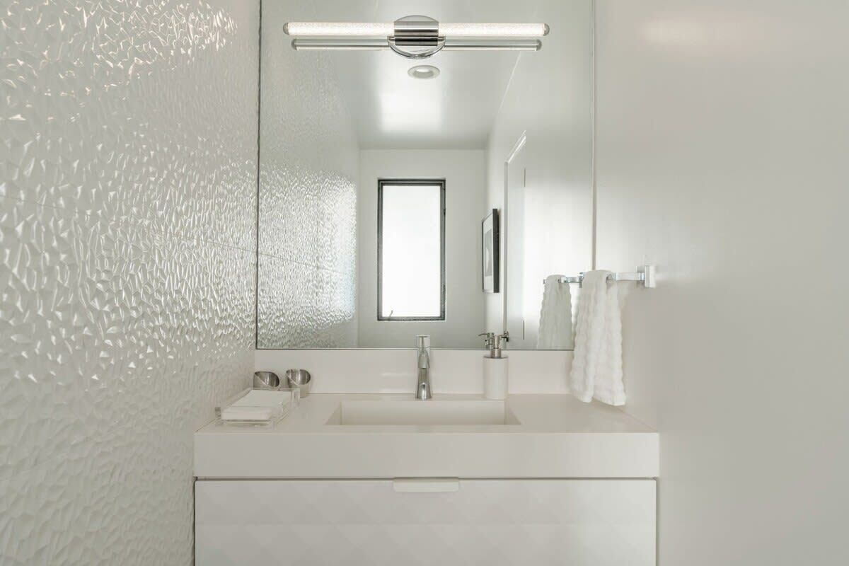 A modern bathroom with a large mirror, a white sink, and a towel rack.