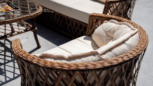 Mobilier en osier avec des coussins, une table avec un plateau en verre et un canapé avec un coussin.