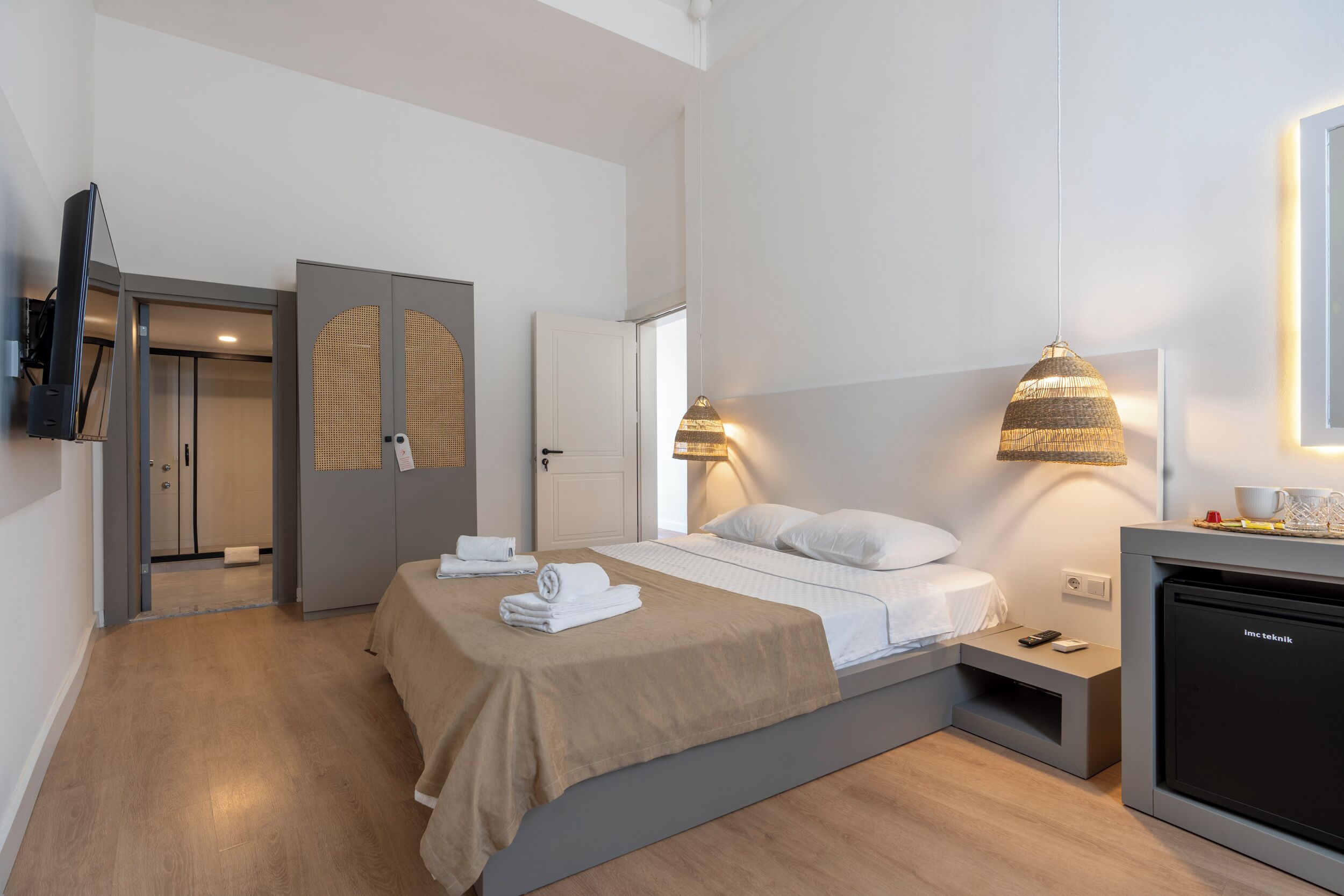 Una habitación de hotel moderna con cama, mesitas de noche, televisor y minibar.