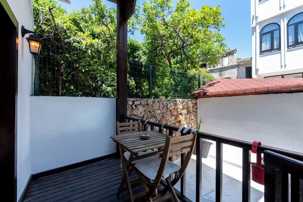 Un balcón con una mesa y sillas de madera, un muro de piedra y vistas a árboles y edificios.