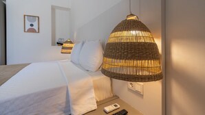 Un lit bien fait, avec du linge de lit blanc, une table de chevet avec une télécommande et un luminaire suspendu en osier.