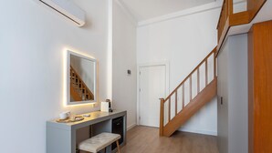 Un couloir moderne avec une console grise, un banc, un miroir et un escalier doté de rampes en bois.