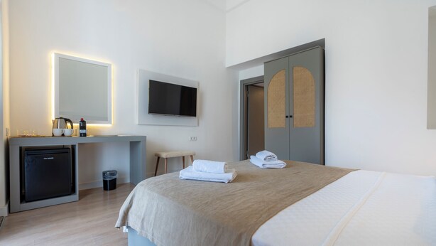 A hotel room with a bed, a desk with a computer and a small fridge, a TV mounted on the wall, and a door with a woven pattern. - My Antalya (Antalya)