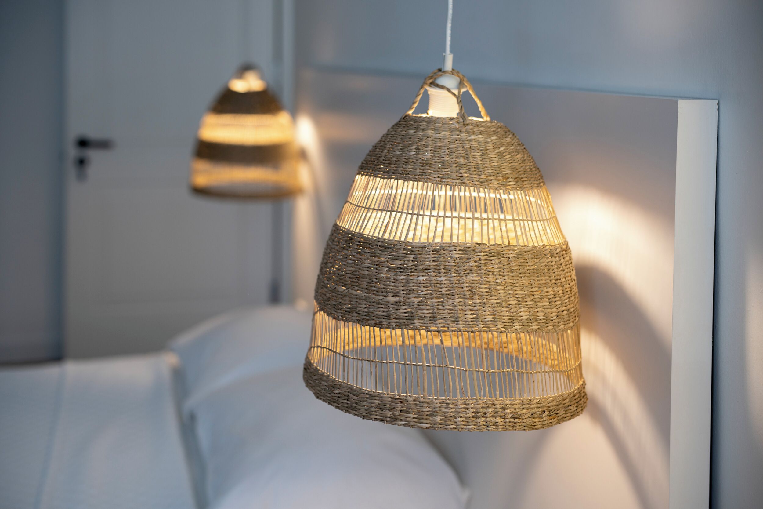 A room with a bed and two hanging wicker lamps.