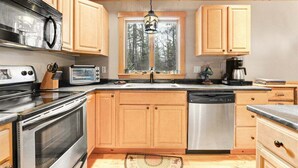 Una cocina con armarios de madera, electrodomésticos de acero inoxidable, un ventanal con vista a árboles y una lámpara colgante.