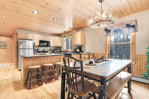 A wooden-paneled kitchen with a central island, bar stools, and a dining table. - Deer Run - Chalet w/ Fireplace (Greenwood)