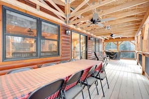 A covered outdoor dining area with a long table and chairs, large windows, and ceiling fans. - Deer Run - Chalet w/ Fireplace (Greenwood)