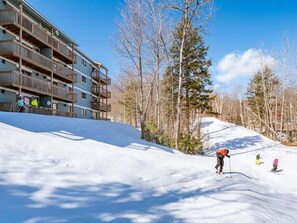 A ski resort with a multi-story building, a snow-covered slope, and trees. - White Cap B-113 - Sunday River Condo (Newry)