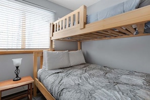 A bunk bed with a wooden frame, a gray patterned bedspread, and a bedside table with a lamp. - White Cap B-113 - Sunday River Condo (Newry)
