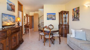 A dining area with a wooden table and chairs, a television on a cabinet, and wall-mounted artwork. - Apartment Bella Sathea (Torri del Benaco)