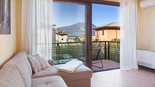 A balcony with a sofa, a glass table with two wine glasses, and a view of a mountain. - Apartment Bella Sathea (Torri del Benaco)